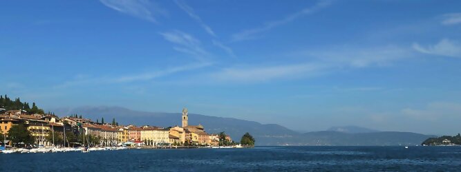 Trip Flüge beliebte Urlaubsziele am Gardasee -  Mit einer Fläche von 370 km² ist der Gardasee der größte See Italiens. Es liegt am Fuße der Alpen und erstreckt sich über drei Staaten: Lombardei, Venetien und Trentino. Die maximale Tiefe des Sees beträgt 346 m, er hat eine längliche Form und sein nördliches Ende ist sehr schmal. Dort ist der See von den Bergen der Gruppo di Baldo umgeben. Du trittst aus deinem gemütlichen Hotelzimmer und es begrüßt dich die warme italienische Sonne. Du blickst auf den atemberaubenden Gardasee, der in zahlreichen Blautönen schimmert - von tiefem Dunkelblau bis zu funkelndem Türkis. Majestätische Berge umgeben dich, während die Brise sanft deine Haut streichelt und der Duft von blühenden Zitronenbäumen deine Nase kitzelt. Du schlenderst die malerischen, engen Gassen entlang, vorbei an farbenfrohen, blumengeschmückten Häusern. Vereinzelt unterbricht das fröhliche Lachen der Einheimischen die friedvolle Stille. Du fühlst dich wie in einem Traum, der nicht enden will. Jeder Schritt führt dich zu neuen Entdeckungen und Abenteuern. Du probierst die köstliche italienische Küche mit ihren frischen Zutaten und verführerischen Aromen. Die Sonne geht langsam unter und taucht den Himmel in ein leuchtendes Orange-rot - ein spektakulärer Anblick.
